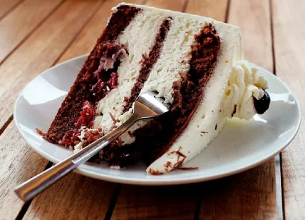 a slice of red velvet cake with cream cheese frosting, cherry filling, and chocolate shavings